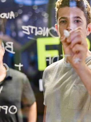 cutting-edge marketing techniques, thoughtful expression, crafting digital campaigns, photorealistic, sophisticated agency with sleek furniture and ambient lighting, highly detailed, interactive touch panels and digital pads, enhanced contrast, deep blues and purples, ambient LED lighting, shot with an 85mm prime lens.